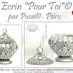 May include: A silver and gray decorative box with a lid, made with beads and a pearl on top. The box is labeled "Ecrin "Pour Toi" par Puca® - Paris".