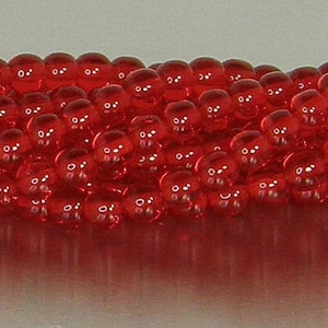 May include: A strand of small, round, red glass beads. The beads are translucent and have a slight shine.