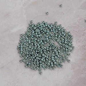 May include: A large pile of silver-colored metal beads on a light gray surface.