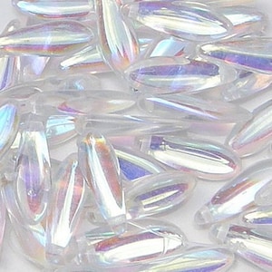 May include: A pile of iridescent white glass beads in an oval shape. The beads have a pearlescent finish and are scattered on a white surface.