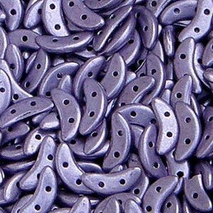 May include: A close-up of a pile of small, crescent-shaped beads. The beads are a deep purple color with a metallic sheen.