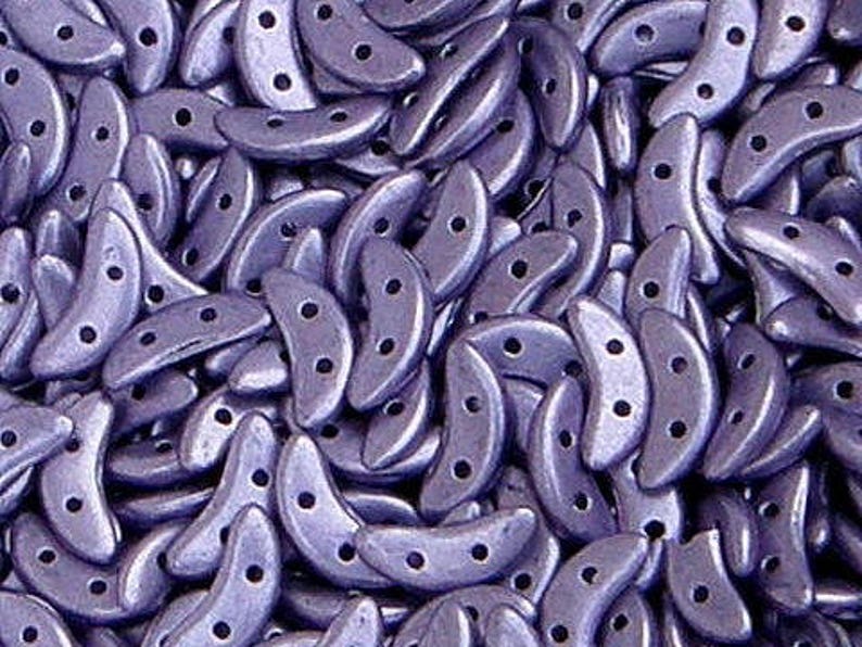 May include: A close-up of a pile of small, crescent-shaped beads. The beads are a deep purple color with a metallic sheen.