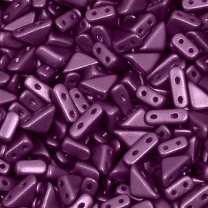 May include: Close-up of a pile of metallic purple beads. The beads are a mix of triangular and rectangular shapes, each with two holes for stringing. The surface of the beads has a matte finish, and the color is a deep, rich purple.