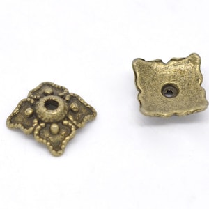 May include: Two antique gold metal square-shaped decorative embellishments with a hole in the center. The embellishments have a detailed design with a raised center and a textured surface.