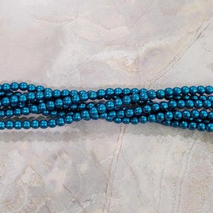 May include: A strand of teal blue round beads. The beads are smooth and have a metallic sheen.