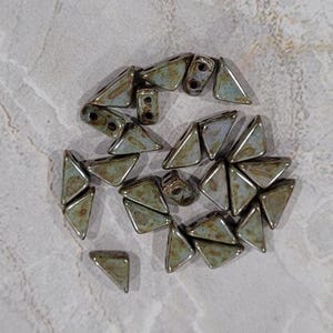 May include: A collection of approximately 20 small, triangular ceramic beads in shades of green and brown. The beads have a mottled, iridescent finish and are arranged in a loose circle.