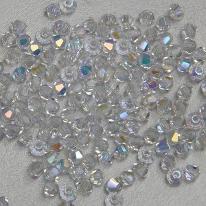 May include: A scattering of clear, faceted crystal beads. The beads display an iridescent sheen, reflecting various colours. The small, round beads are ideal for jewellery making or other craft projects.