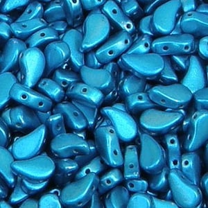 May include: A close-up shot of a pile of shiny, teal-colored beads. The beads are teardrop and rectangular shapes with holes for stringing. The beads have a metallic sheen, reflecting light.