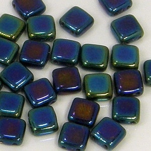 May include: A collection of iridescent blue square glass beads. The beads have a dark blue, green, and purple color shift.