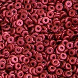 May include: A close-up view of a large quantity of small, red, donut-shaped beads. The beads have a metallic sheen and are arranged in a random pattern.