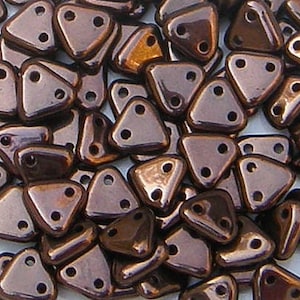 Op de afbeelding: Een grote hoeveelheid kleine, driehoekige, bruine glazen kralen met elk twee gaten. De kralen hebben een metallic glans.