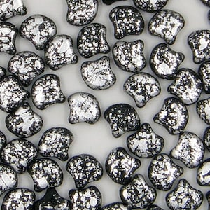May include: A close-up of a group of silver and black glass beads. The beads are shaped like a crescent moon and have a speckled, textured surface.