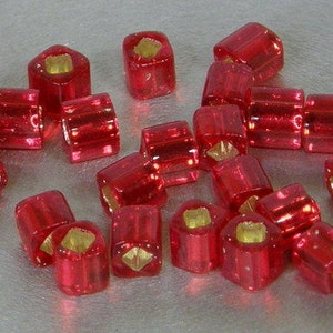 May include: A collection of red glass beads with gold accents. The beads are square shaped and have a shiny finish.