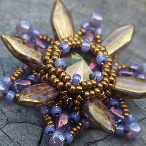 May include: A beaded flower brooch with a large iridescent purple crystal in the center. The flower has six petals and is surrounded by smaller purple and gold beads.