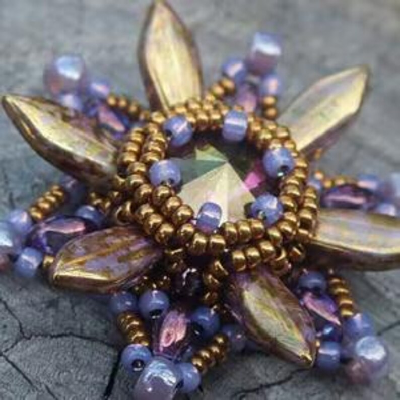 May include: A beaded flower brooch with a large iridescent purple crystal in the center. The flower has six petals and is surrounded by smaller purple and gold beads.