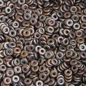 May include: A close-up shot of a pile of small, metallic, donut-shaped beads. The beads have a bronze and silver color, with a hole in the center. The beads are scattered and piled together, creating a textured surface.