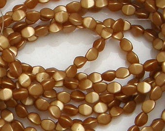 Könnte beinhalten: Nahaufnahme von Strängen goldbrauner, flacher, ovaler Perlen. Jede Perle hat einen zweifarbigen Effekt mit einem helleren, fast cremefarbenen Abschnitt. Die Perlen sind aufgefädelt, ideal für Schmuck.