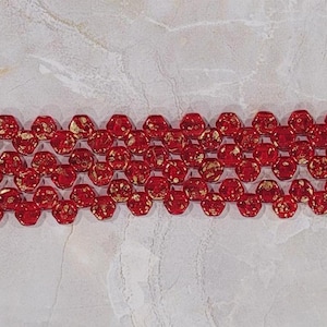 May include: Red hexagonal glass beads with gold flecks. The beads are strung together in a long strand.