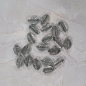 May include: A collection of silver leaf-shaped charms. The charms are all the same size and shape, and they have a detailed leaf design.