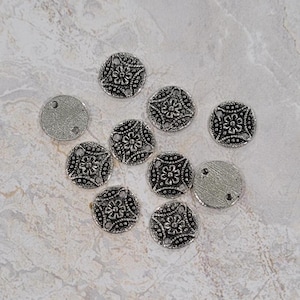 May include: A collection of silver-toned metal charms with intricate floral designs. The charms are round and have a slightly raised center with a floral pattern.