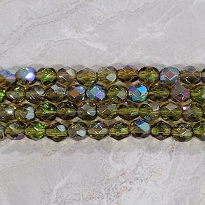 May include: A strand of iridescent green faceted glass beads. The beads are round and have a diamond-like cut.
