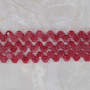 May include: A strand of red glass beads with a hexagonal shape and a textured surface.