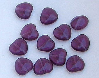 May include: A collection of twelve purple glass heart-shaped beads. The beads have a slightly iridescent finish.