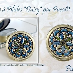 May include: A gold pill box with a blue, green, and gold floral design. The box is labeled "Boite à Pilules "Daisy" par Puca®-Paris".