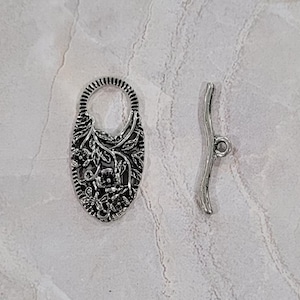 May include: Silver-toned metal clasp with a floral design and a matching toggle clasp. The clasp is oval-shaped and has a delicate floral pattern.