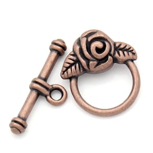 May include: A copper-toned metal toggle clasp with a rose design. The clasp has a round ring and a bar with a small loop.
