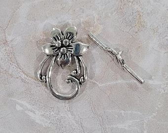 May include: Silver-toned metal flower charm with a decorative swirl design and a matching silver-toned metal toggle clasp.