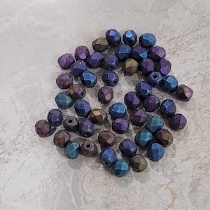 May include: A pile of iridescent blue and purple glass beads. The beads are faceted and have a metallic sheen.
