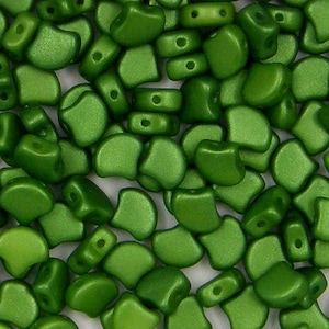 May include: A close-up of a pile of green glass beads. The beads are shaped like a crescent moon and have a matte finish.
