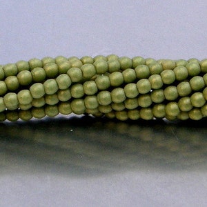 May include: Close-up of a strand of olive green wooden beads. The beads are round and evenly spaced, creating a textured surface. The beads have a matte finish and are strung together, suitable for jewelry making or craft projects.
