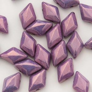 May include: A group of small, iridescent purple diamond-shaped beads. The beads have a metallic sheen and are scattered on a white surface.