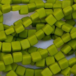 May include: A strand of lime green square glass beads. The beads are opaque and have a matte finish.