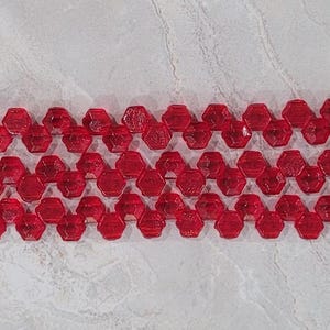 May include: A strand of red glass beads, each bead is shaped like a hexagon with a faceted surface.