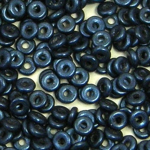 May include: A close-up shot of a pile of small, dark blue wooden beads. Each bead is ring-shaped with a hole in the center. The beads are scattered, creating a textured surface. The color is a deep, saturated blue.
