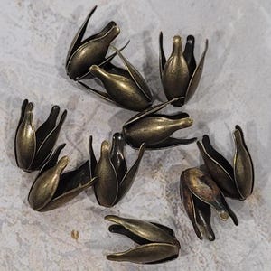 May include: A group of ten antique gold metal flower-shaped bead caps. The caps are made of metal and have a slightly textured finish.
