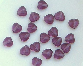 May include: A collection of purple heart-shaped glass beads. The beads are translucent and have a slight shimmer.