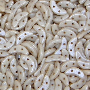 May include: A close-up of a pile of off-white, crescent-shaped glass beads with three holes each. The beads have a subtle iridescent sheen.