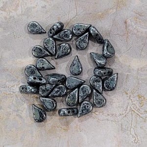 Puede incluir: Una colección de cuentas de vidrio gris oscuro en forma de lágrima. Las cuentas tienen una superficie moteada y texturizada.