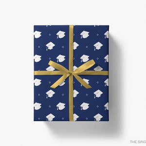 May include: A navy blue gift wrap with a white graduation cap pattern. The gift wrap is tied with a gold ribbon.
