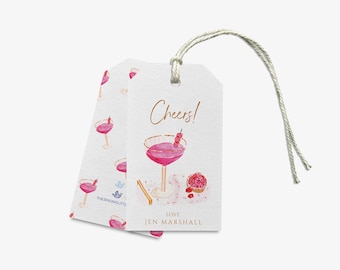 Può includere: Un'etichetta regalo bianca con un'illustrazione di cocktail rosa e il testo "Cheers! Love Jen Marshall".