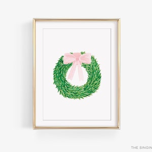 May include: A green wreath with a pink bow on a white background. The wreath is in a gold frame.