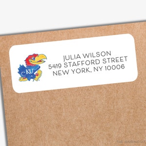 May include: A white address label with a blue and red cartoon mascot with the letters "KU" on its chest. The text on the label reads "JULIA WILSON 5419 STAFFORD STREET NEW YORK, NY 10006".