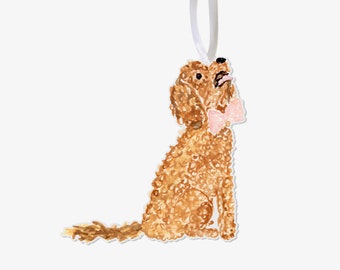 Pode incluir: Enfeite de cachorro em estilo aquarela com pelo castanho claro e laço rosa. O cachorro está sentado e olhando para cima, preso a uma fita branca para pendurar. Um item decorativo charmoso.