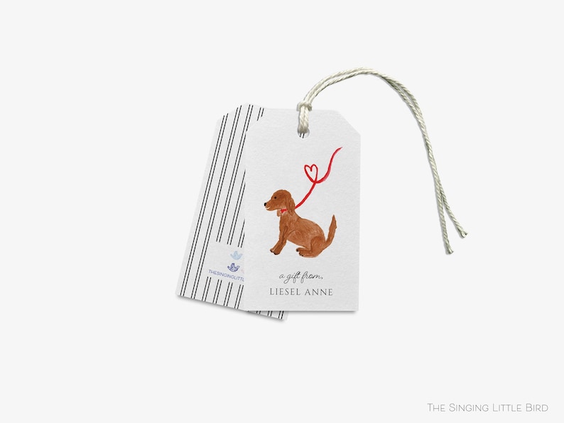 May include: A white gift tag with a brown dog illustration and a red heart-shaped leash. The text "a gift from... Liesel Anne" is printed on the tag.
