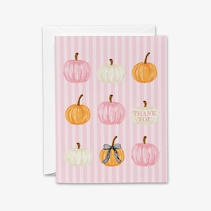 A pink striped card with nine pumpkins of various sizes and colors, including white, orange, and black bows, arranged in a grid pattern.