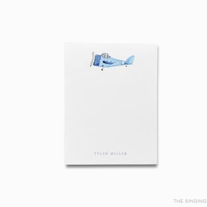 Op de afbeelding: Een witte kaart met een blauwe vliegtuigillustratie en de tekst "Tyler Miller" in grijs gedrukt.